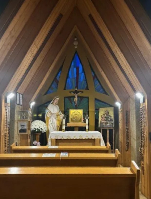 Photo of the interior of a wooden chapel with a tabernacle in the center and devotional images and objects on either side
