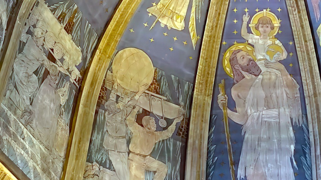 Closeup of a fresco showing St. Christopher bearing the child Jesus, and to the left, travelers bearing a train, an airplane, and a hot-air balloon