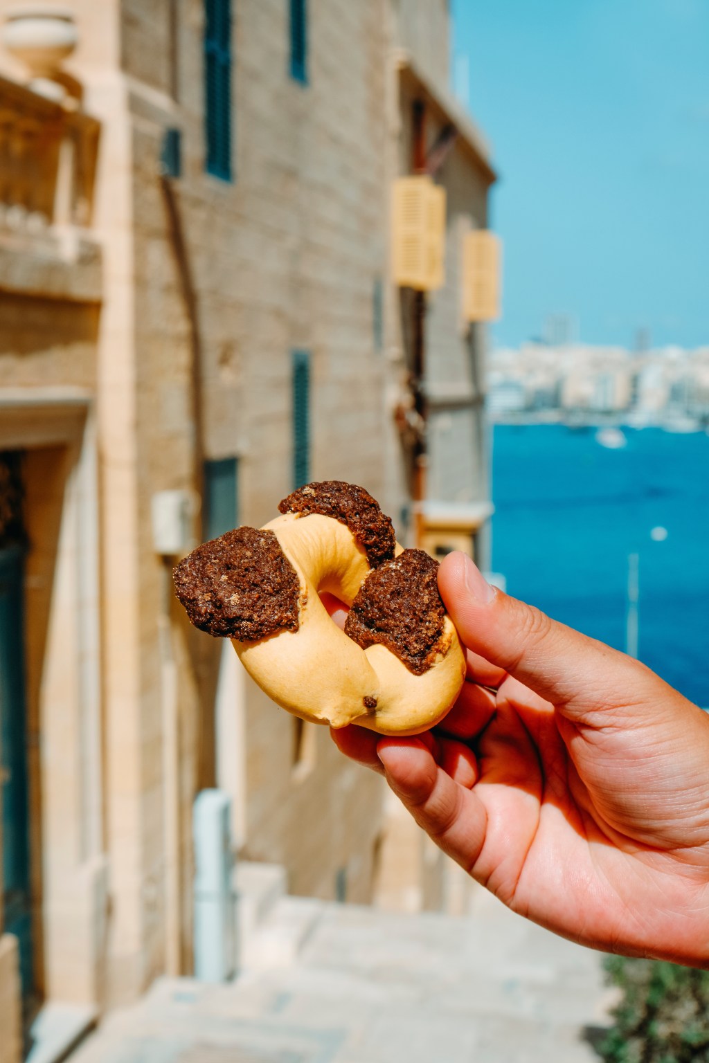 closeup of a man holding a qaghaq tal-ghasel, also known as honey ring in English, typical of Malta, on the street in the old town of Valletta, Malta, on a summer day