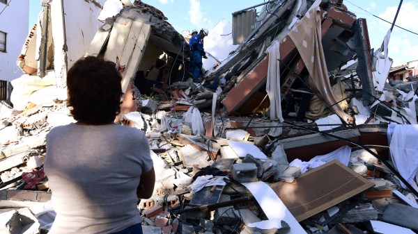A woman looks at rescuers searching for survivors amid the rubble of a collapsed building after an earthquake in Pereira, Colombia on August 10, 2026. A magnitude 7.4 earthquake struck Colombia on August 10, 2026, and killed at least 111 people, damaged more than 1,500 buildings, and left an unknown number of people buried under rubble. The government declared a state of emergency to attend to the quake that shook several cities across the coffee-producing region, the Pacific coast, and neighboring Latin American countries, sending terrified residents racing into the street.