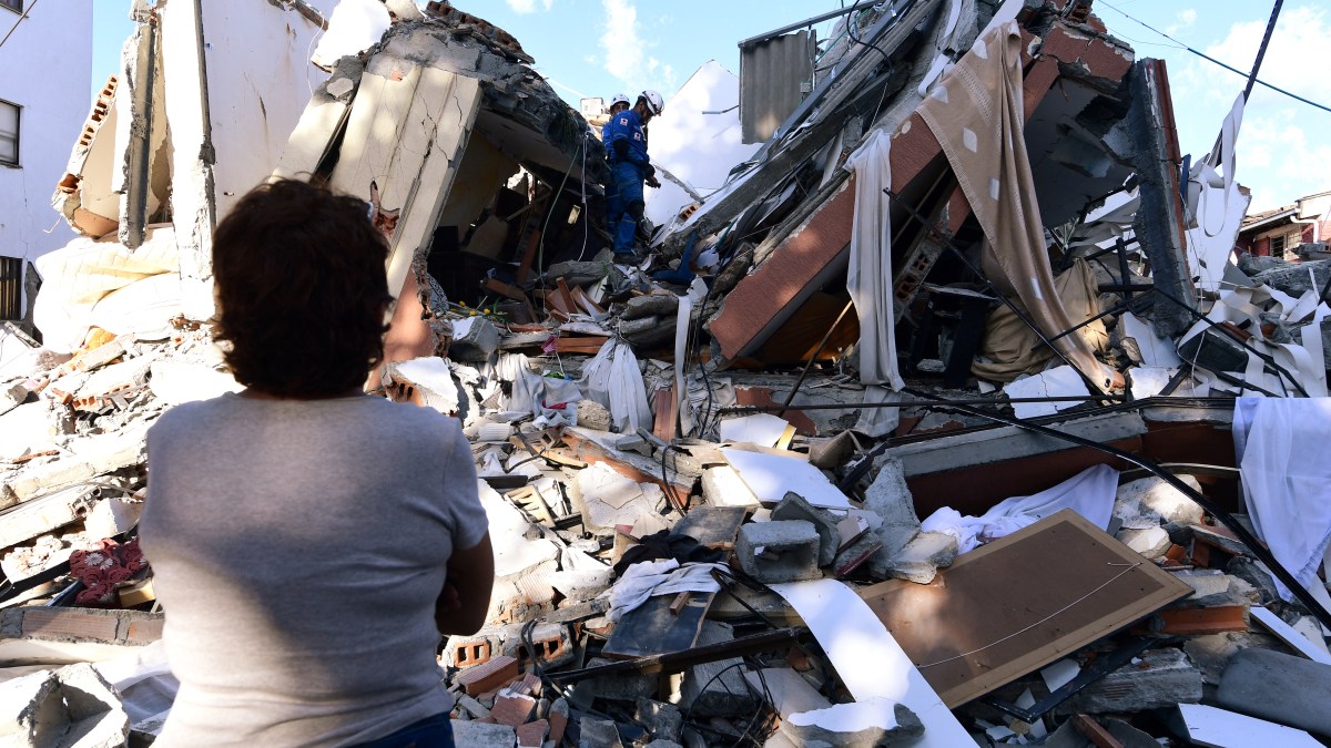 A woman looks at rescuers searching for survivors amid the rubble of a collapsed building after an earthquake in Pereira, Colombia on August 10, 2026. A magnitude 7.4 earthquake struck Colombia on August 10, 2026, and killed at least 111 people, damaged more than 1,500 buildings, and left an unknown number of people buried under rubble. The government declared a state of emergency to attend to the quake that shook several cities across the coffee-producing region, the Pacific coast, and neighboring Latin American countries, sending terrified residents racing into the street.