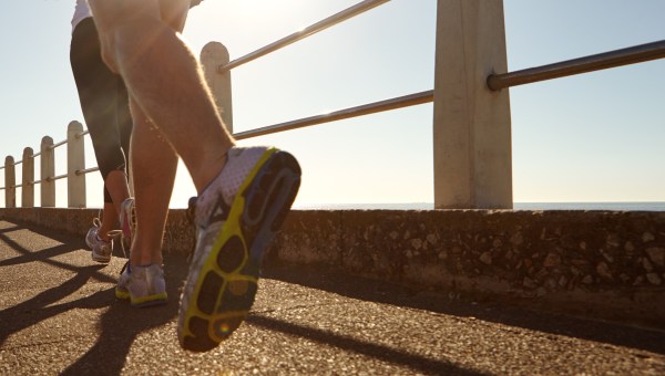 Pareja, piernas y correr con sol en el paseo marítimo para hacer ejercicio, ejercicio cardiovascular o entrenamiento al aire libre. Personas activas, o corredores con zapatos o zapatillas de deporte para la actividad física, la salud o el bienestar